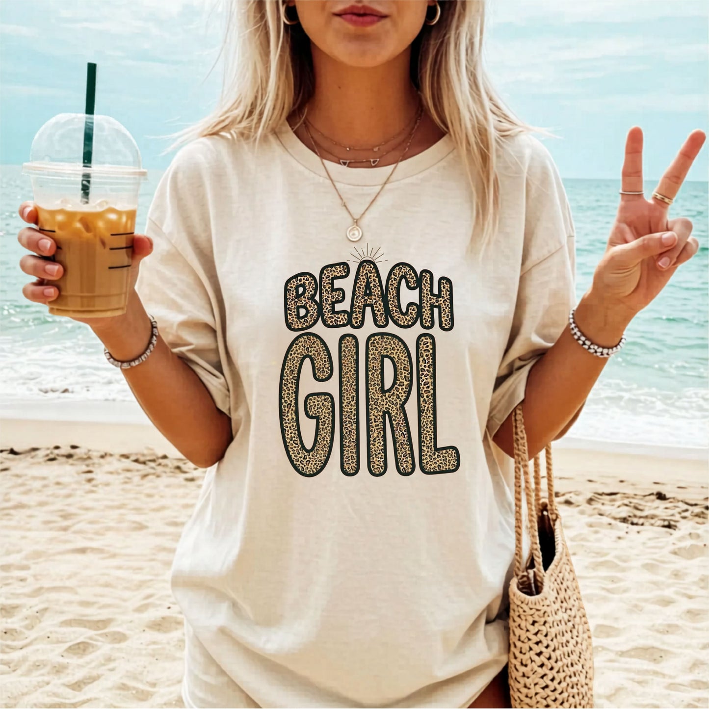 Woman on a beach wearing a 'Beach Girl' Ivory colored t-shirt, holding a drink.