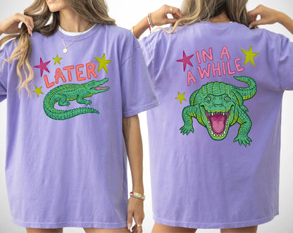 violet t-shirts with alligator graphics on front "later gator" and the text on back i"n a while crocodile"a plain background