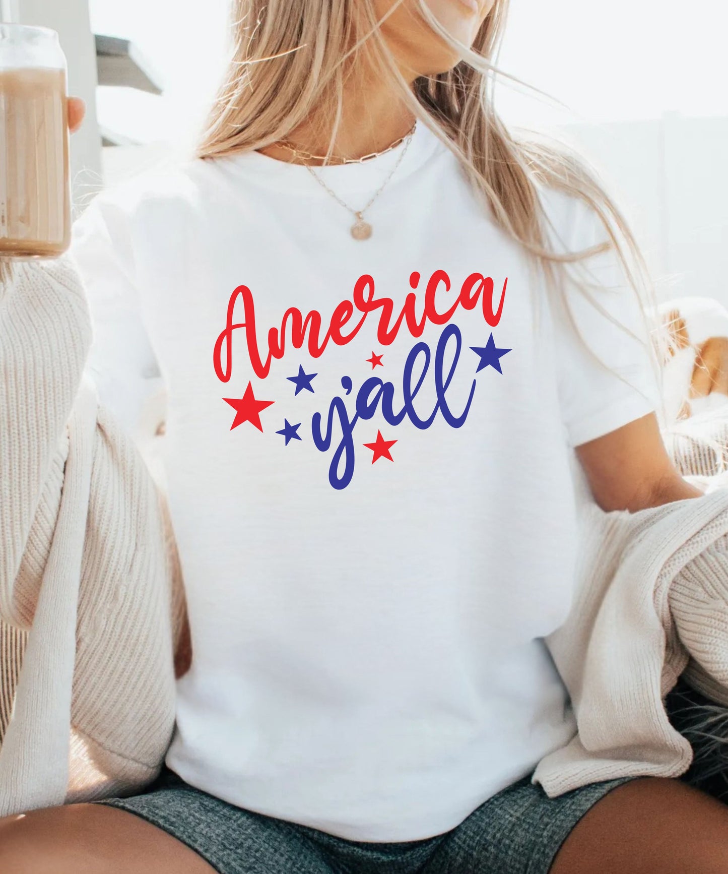 Person wearing a white t-shirt with 'America y'all' text and stars, sitting on a couch.