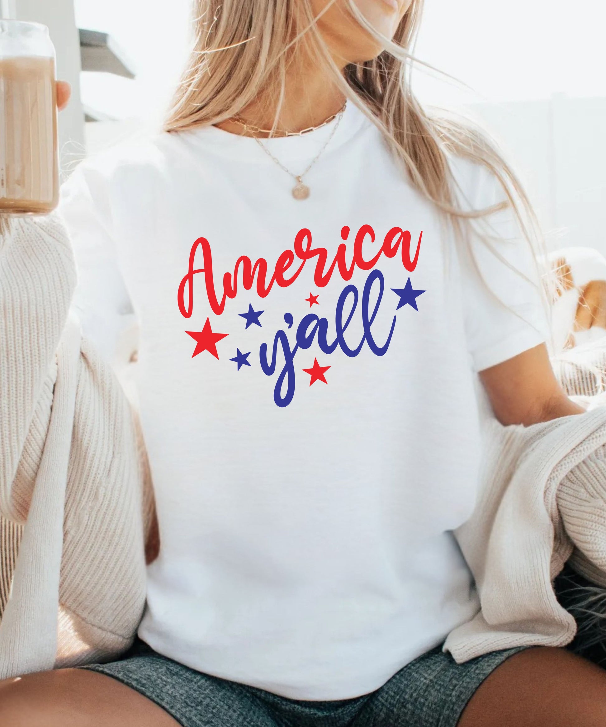 Person wearing a white t-shirt with 'America y'all' text and stars, sitting on a couch.