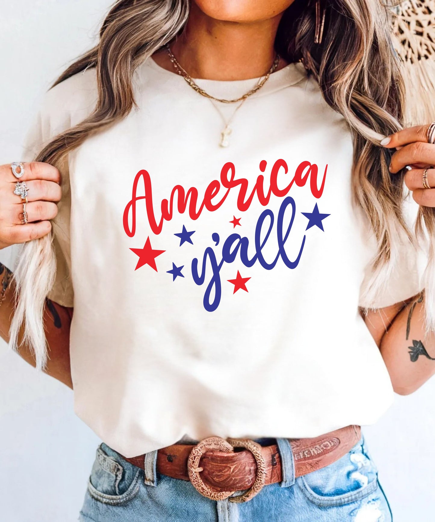Person wearing an ivory t-shirt with 'America y'all' text and red and blue stars.