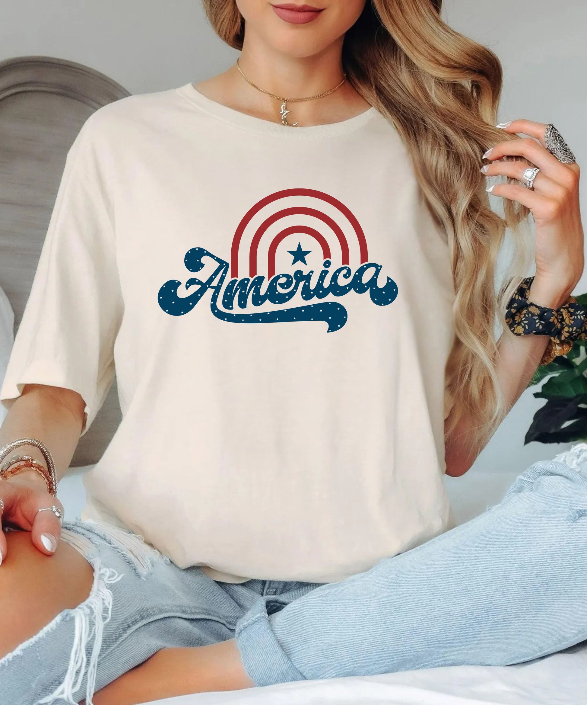 Person wearing an ivory  white t-shirt with 'America' graphic design.