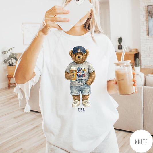 Person wearing a white t-shirt with a bear graphic holding iced coffee, in a living room setting.
