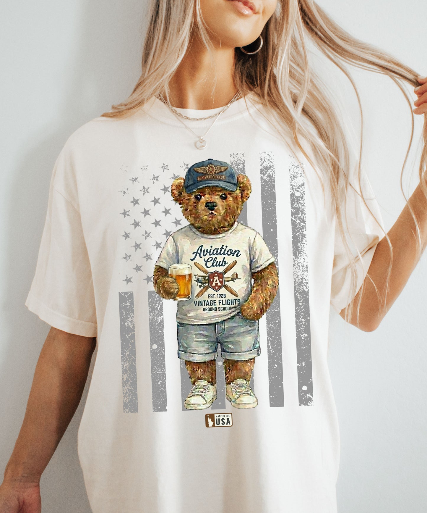 Person wearing an ivory t-shirt with a bear graphic and 'Aviation Club' text against a plain background