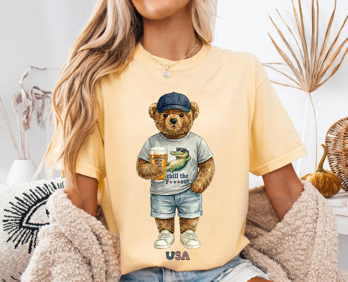 Person wearing a banana t-shirt with a bear graphic holding a beer, sitting in a cozy room.