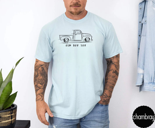 Person wearing a light blue t-shirt with a graphic design of old truck , standing against a white wall.