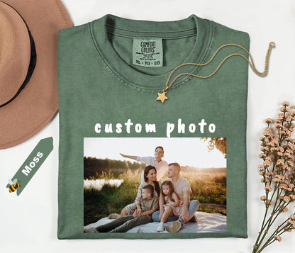 moss t-shirt with a family photo printed on it, placed on a white surface with a hat and dried flowers.