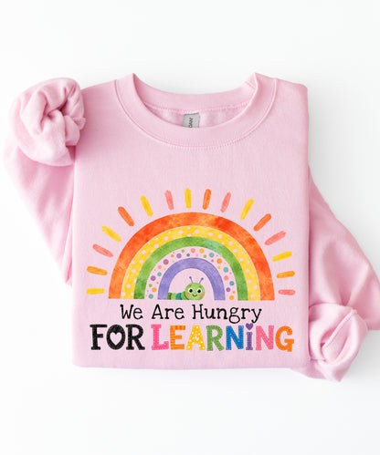 a light pink sweatshirt with a rainbow and text that says we are hungry for learning design.