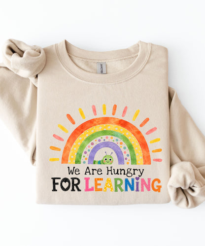 a sand sweatshirt with a rainbow and text that says we are hungry for learning design.