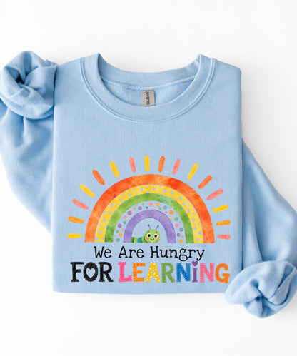 a light blue sweatshirt with a rainbow and text that says we are hungry for learning design.