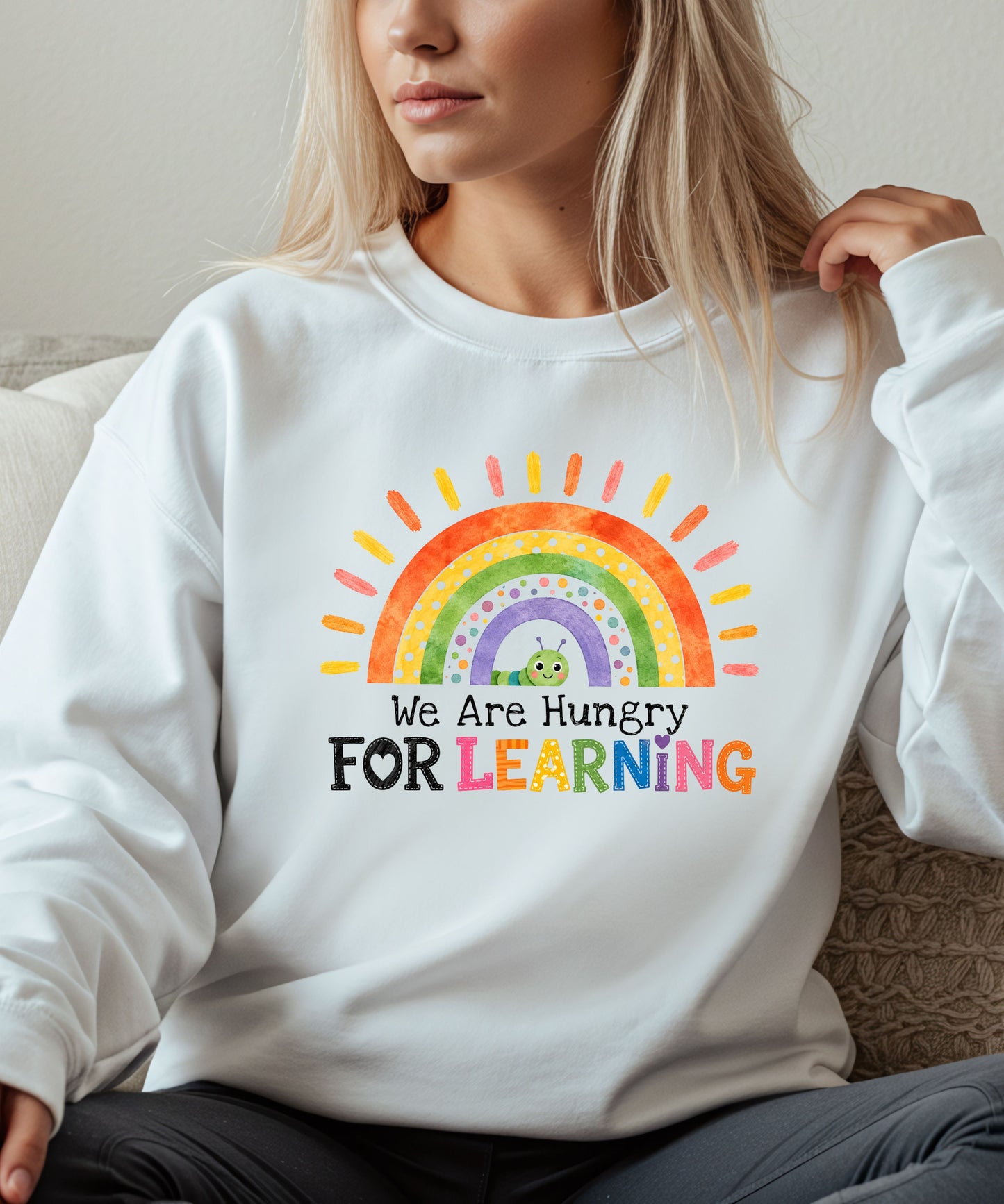 Person wearing a white sweatshirt with a rainbow and text that says we are hungry for learning design.