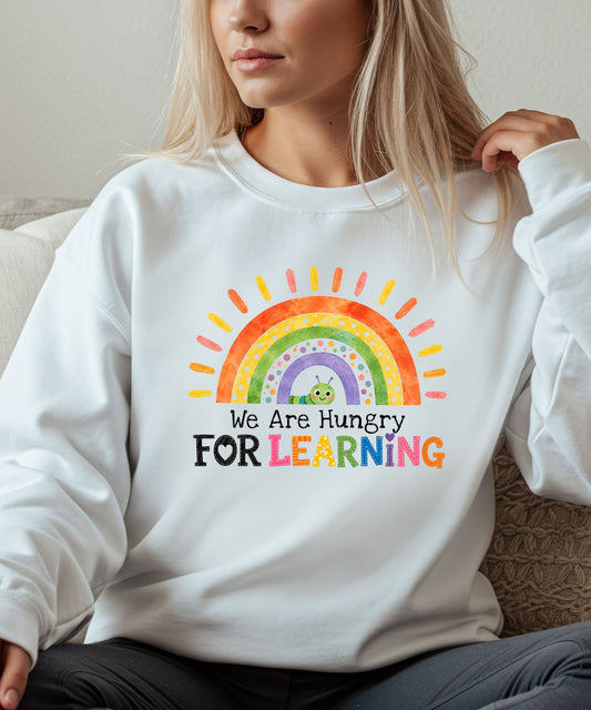 Person wearing a white sweatshirt with a rainbow and text that says we are hungry for learning design.