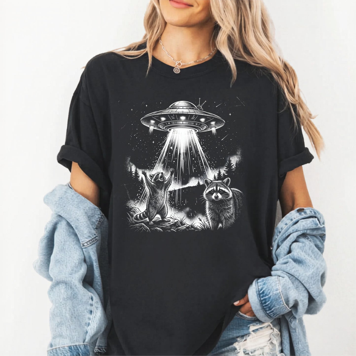 Person wearing a black t-shirt with a graphic of a UFO and raccoons on a white background