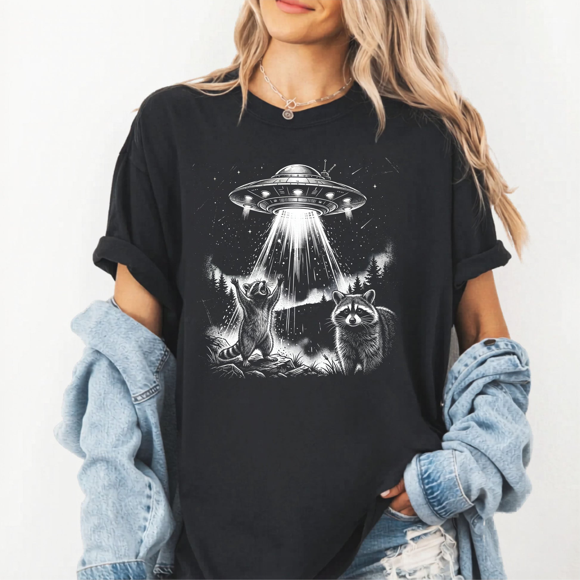 Person wearing a black t-shirt with a graphic of a UFO and raccoons on a white background