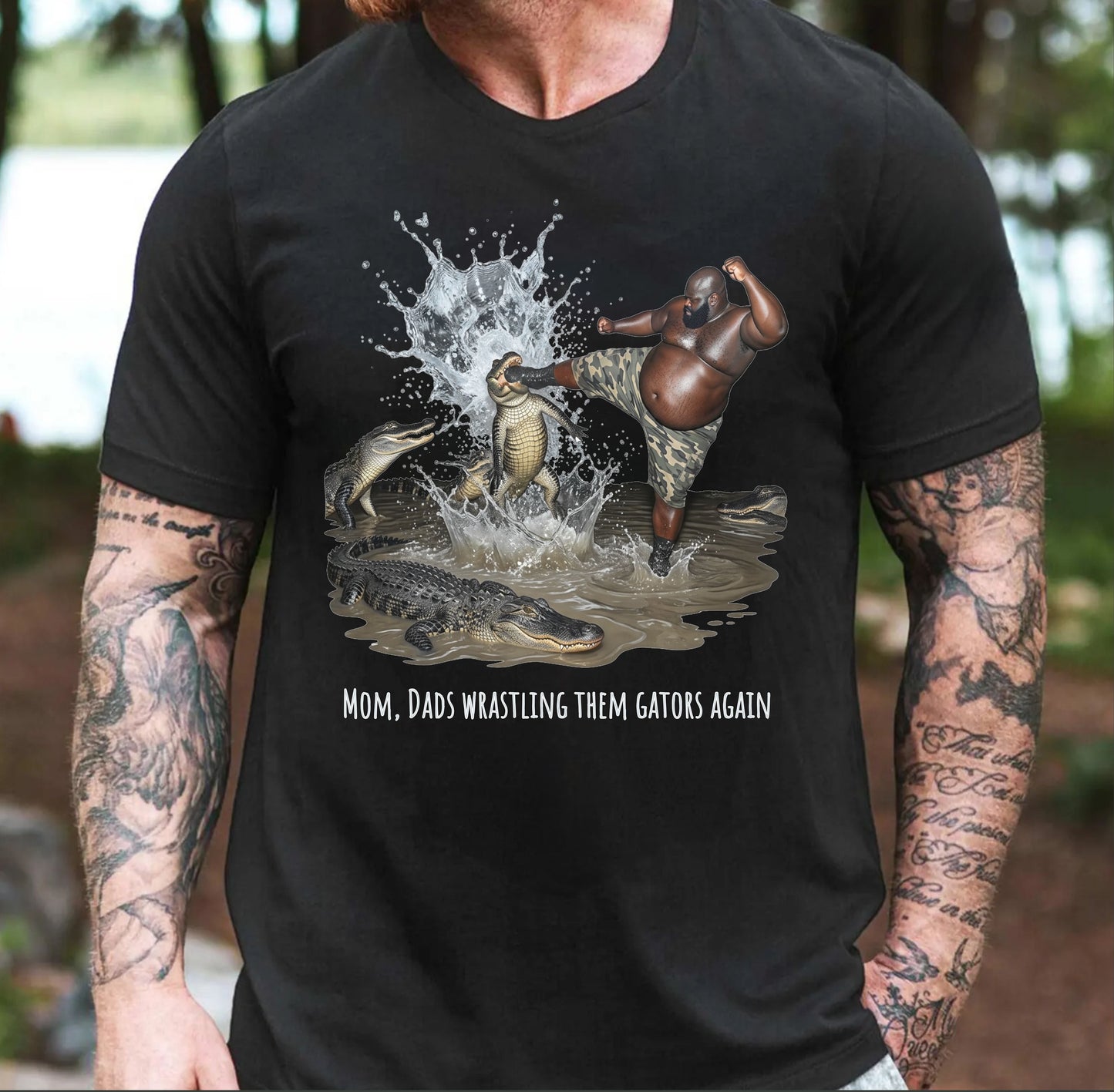 Black t-shirt with graphic design of one person wrestling alligators and text "mom, dad wrastling them gators again" worn by a person with tattoo