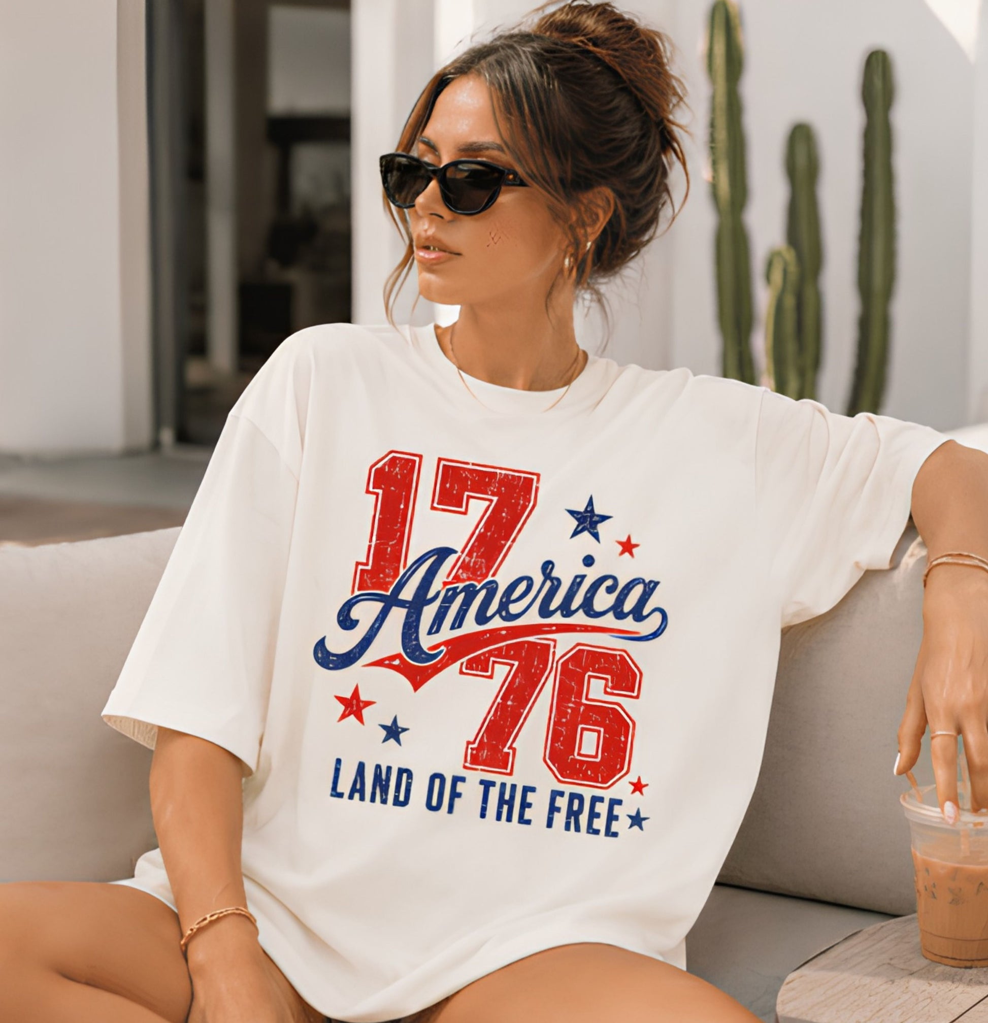Woman wearing a white t-shirt with '17 America 76 Land of the Free' design, sitting on a couch.