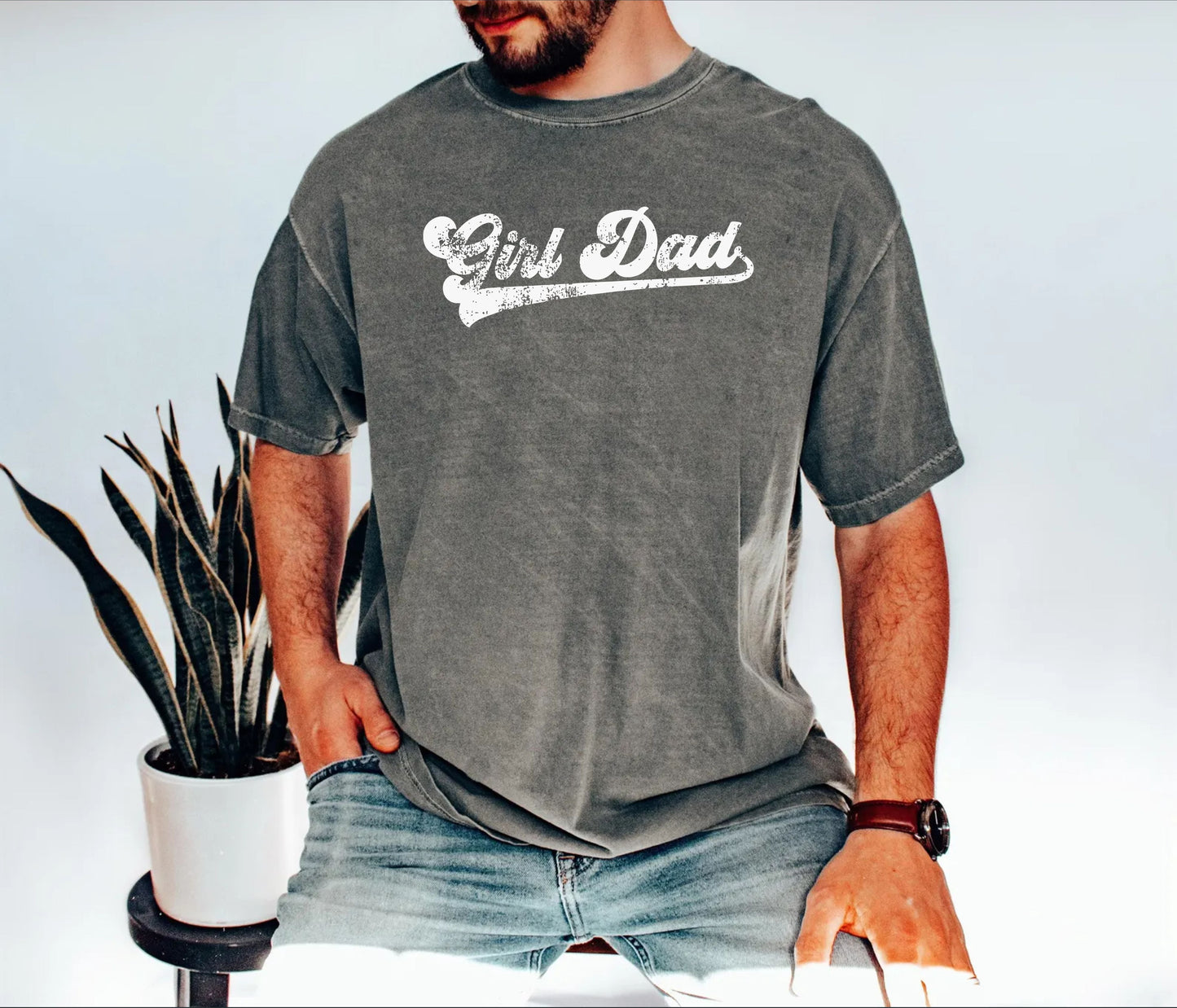 Person wearing a pepper t-shirt with 'Girl Dad' text, standing next to a plant.