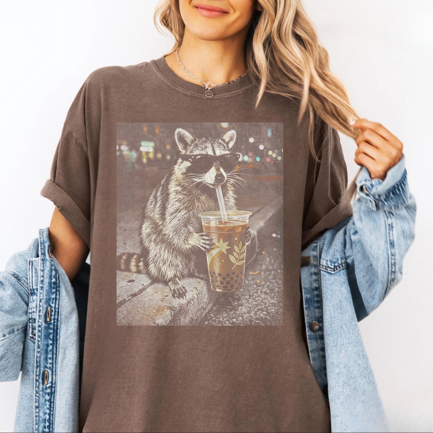 Person wearing an espresso t-shirt with a raccoon graphic drinking from a cup on a white background