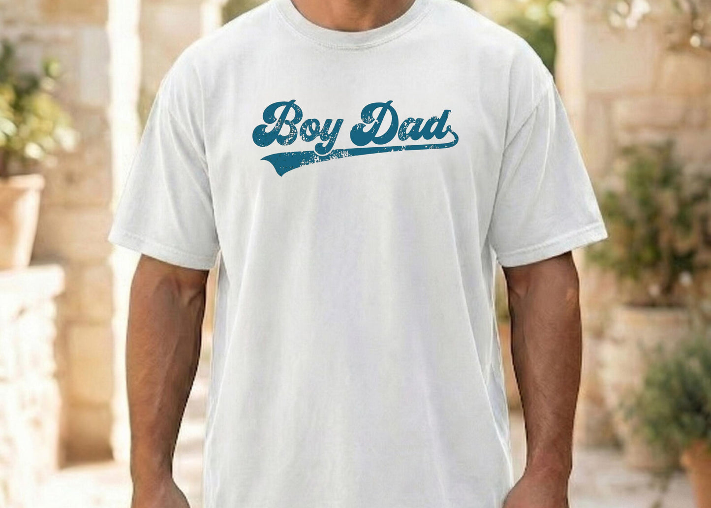 Person wearing a white t-shirt with 'Boy Dad' text in blue outdoors.