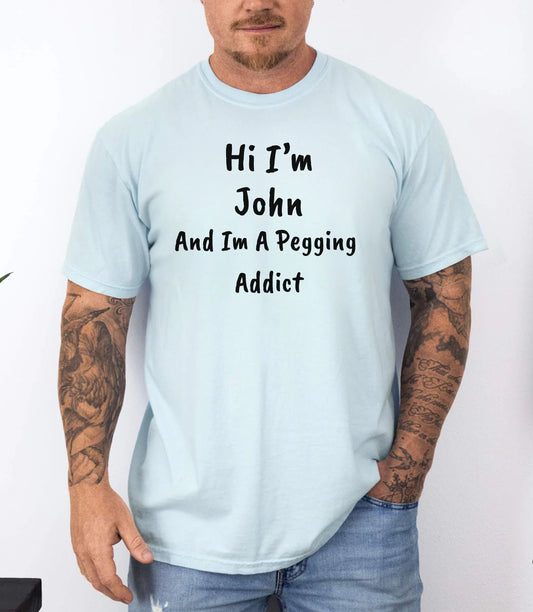 Chambray garment-dyed heavyweight t-shirt with personalized 'Hi I'm [Name] And I'm A Pegging Addict' graphic in handwritten-style font, centered on chest