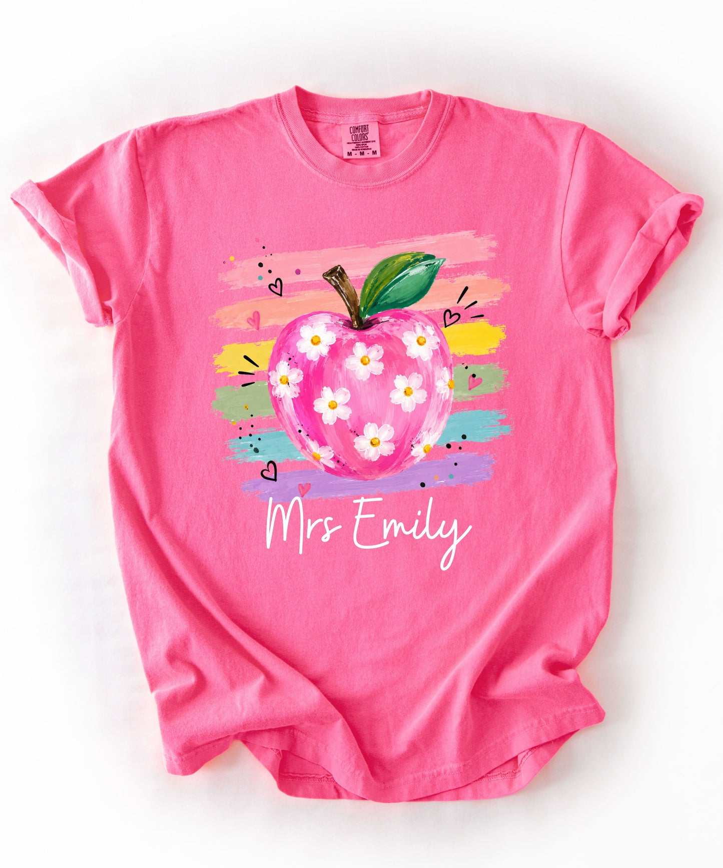 Personalized teacher t-shirt in Neon Pink with floral apple graphic and colorful brushstroke stripes, custom name in script — garment-dyed cotton tee