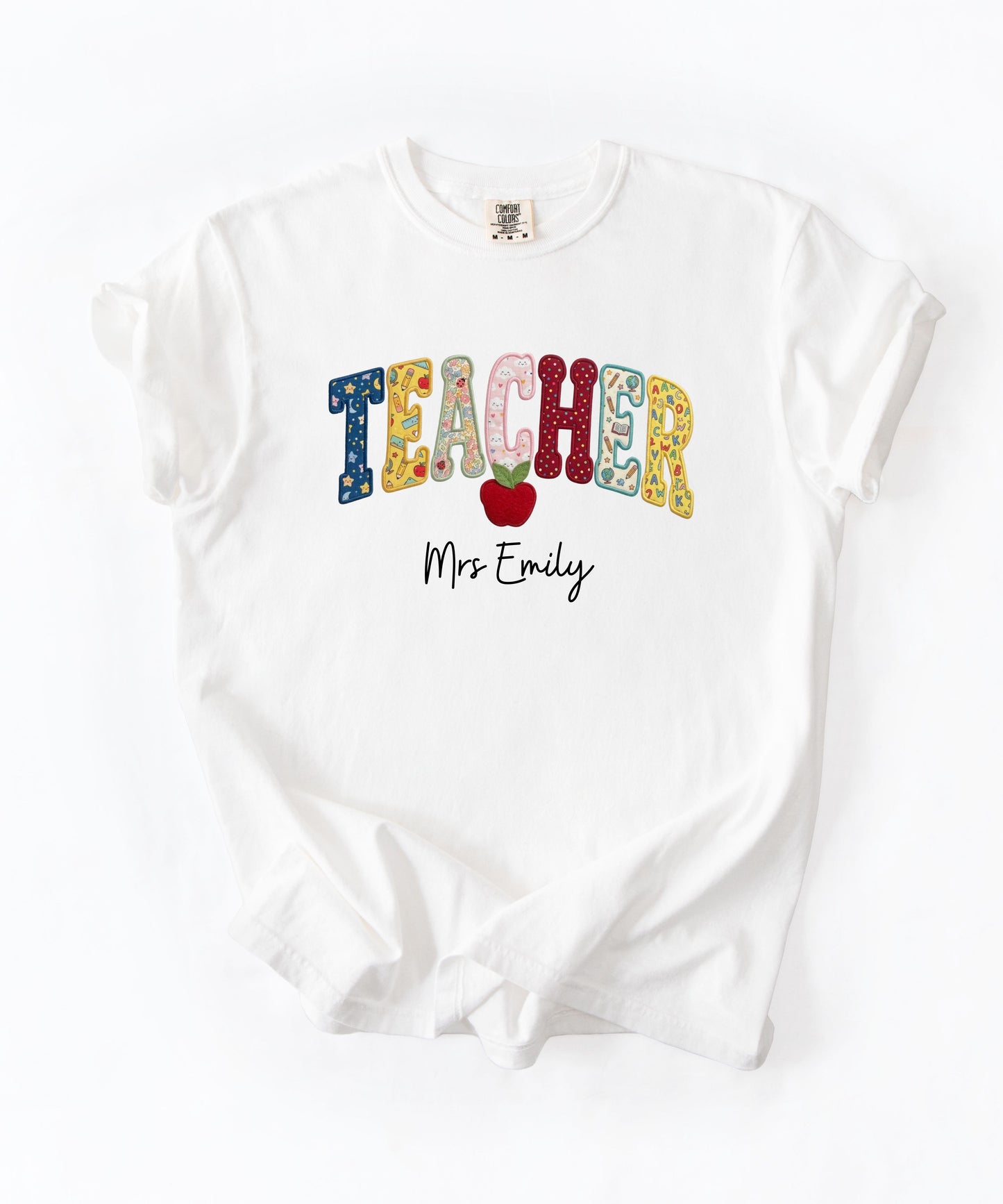 Personalized teacher shirt in White with faux patchwork TEACHER lettering, red apple graphic, and custom name — garment-dyed heavyweight tee
