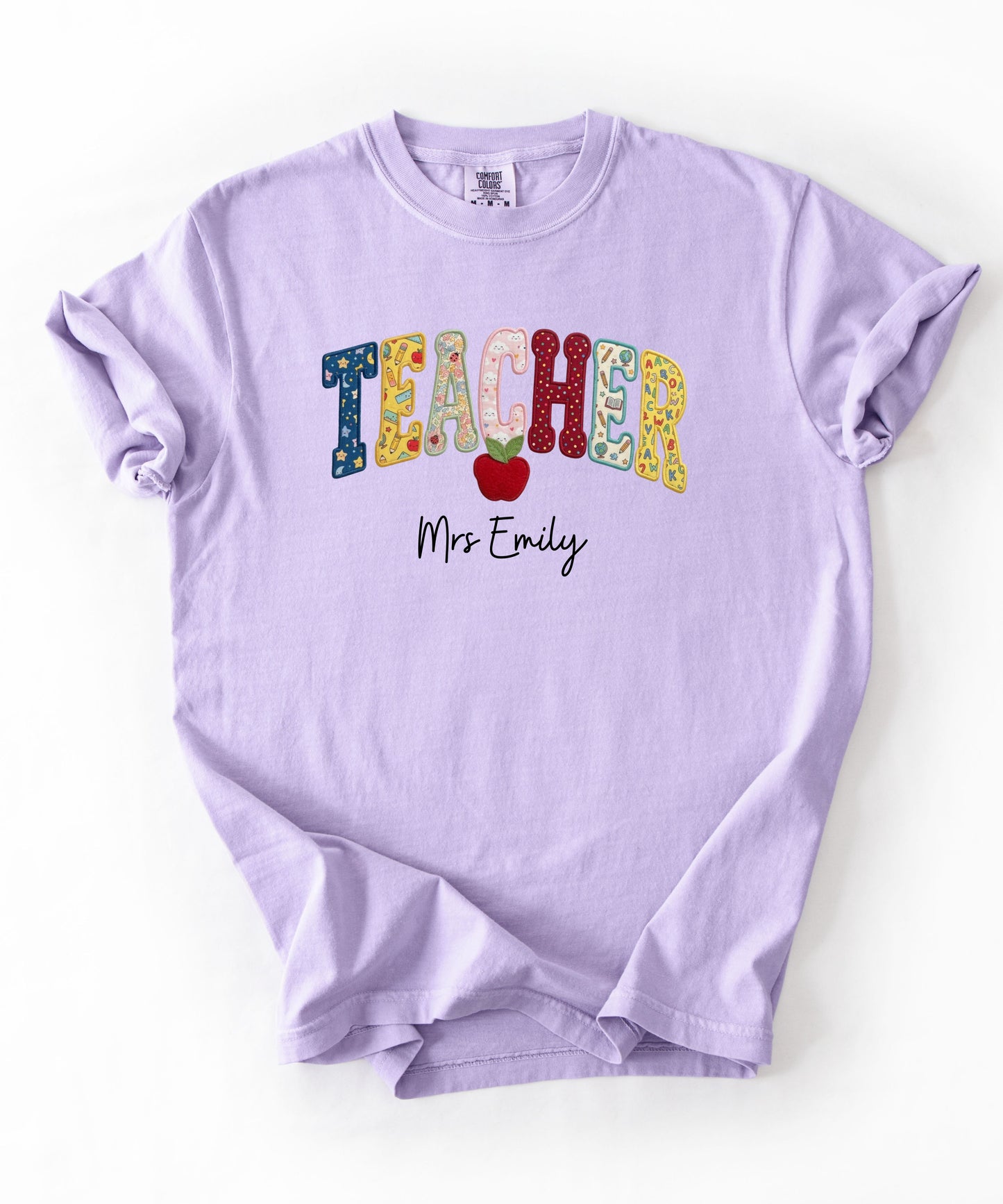 Personalized teacher shirt in Orchid with faux patchwork TEACHER lettering, red apple graphic, and custom name — garment-dyed heavyweight tee