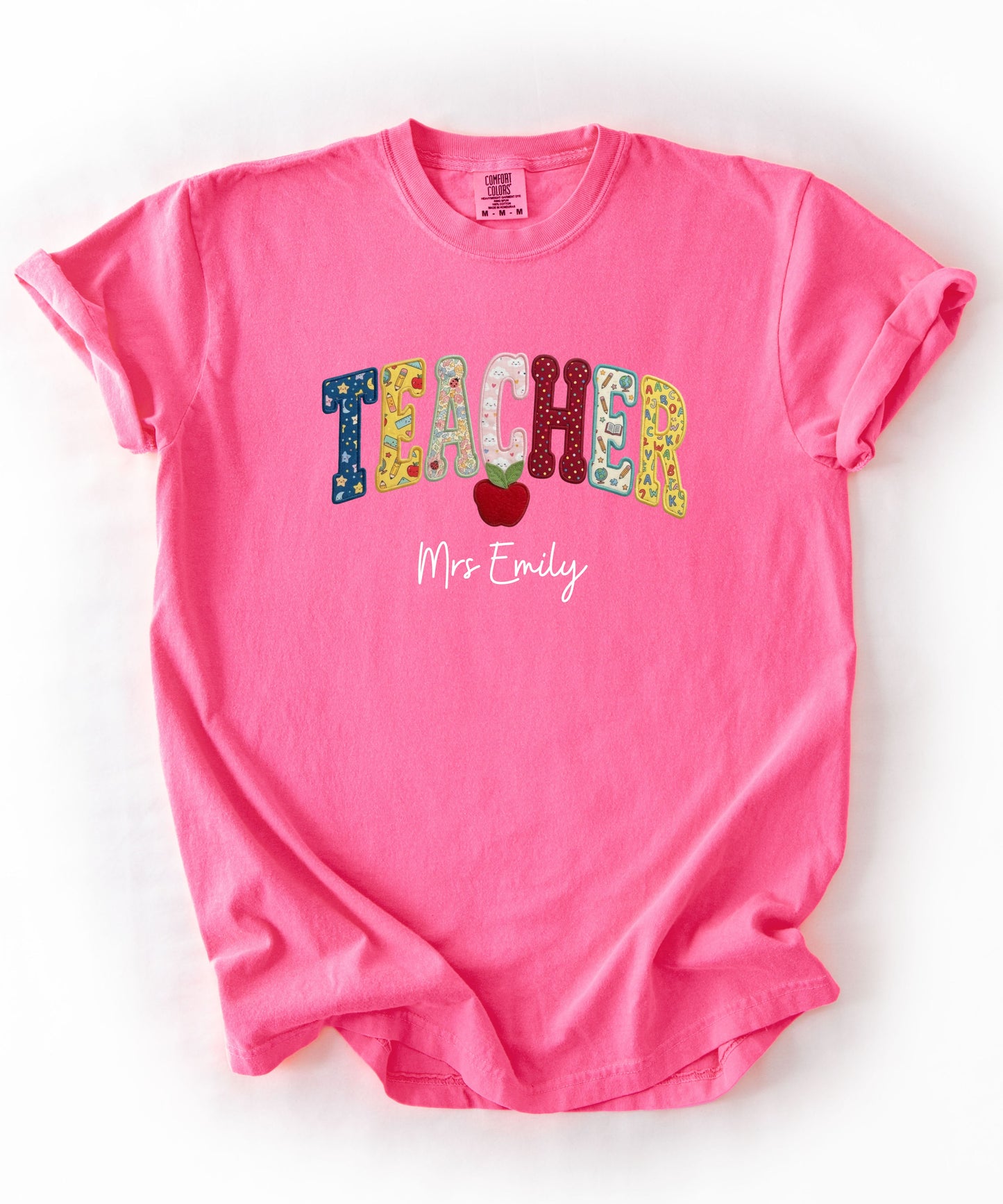 Personalized teacher shirt in Neon Pink with faux patchwork TEACHER lettering, red apple graphic, and custom name — garment-dyed heavyweight tee