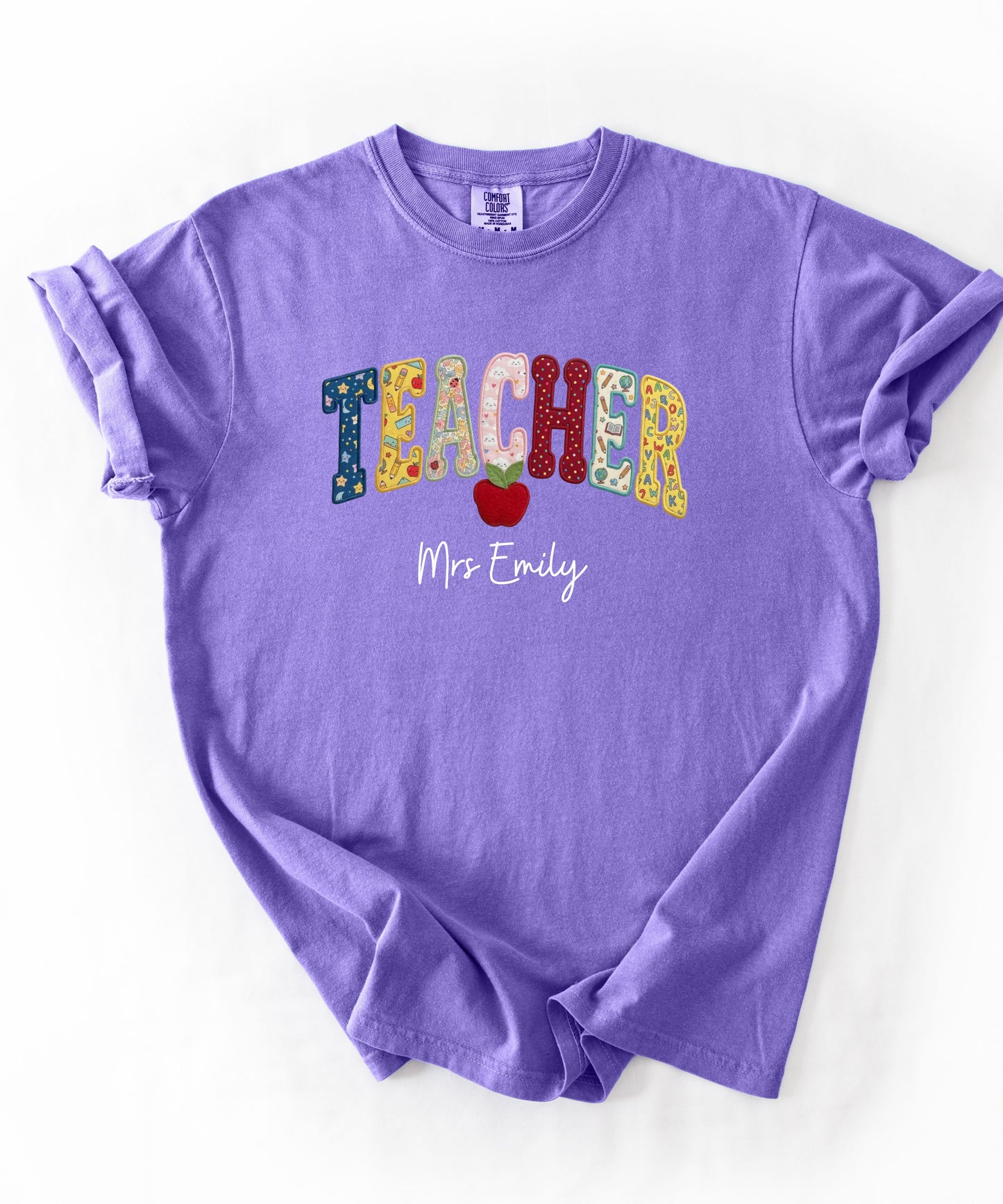 Personalized teacher shirt in Violet with faux patchwork TEACHER lettering, red apple graphic, and custom name — garment-dyed heavyweight tee
