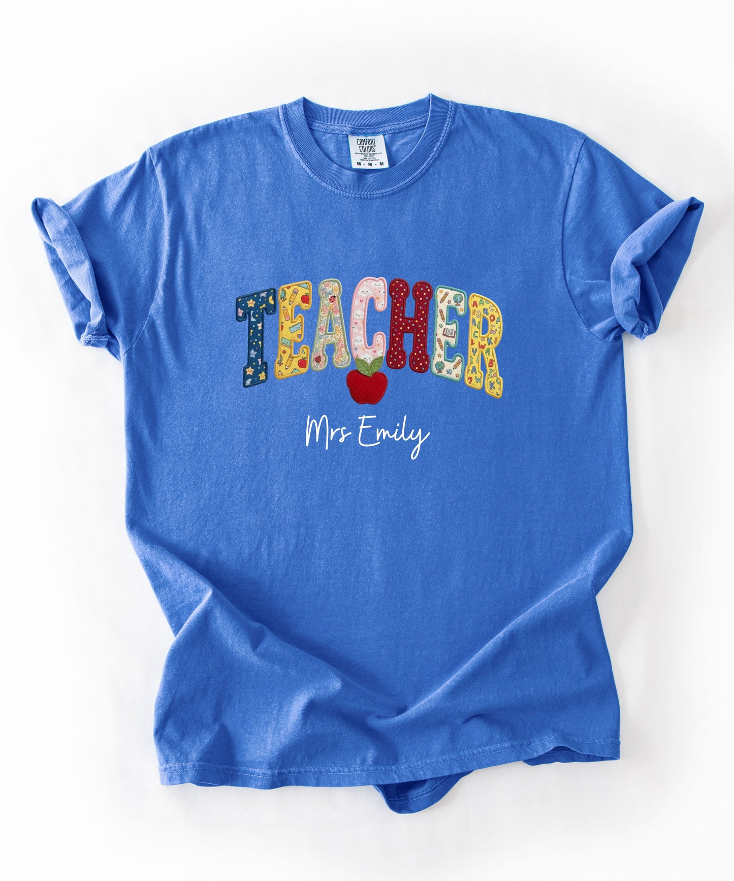 Personalized teacher shirt in Flo Blue with faux patchwork TEACHER lettering, red apple graphic, and custom name — garment-dyed heavyweight tee