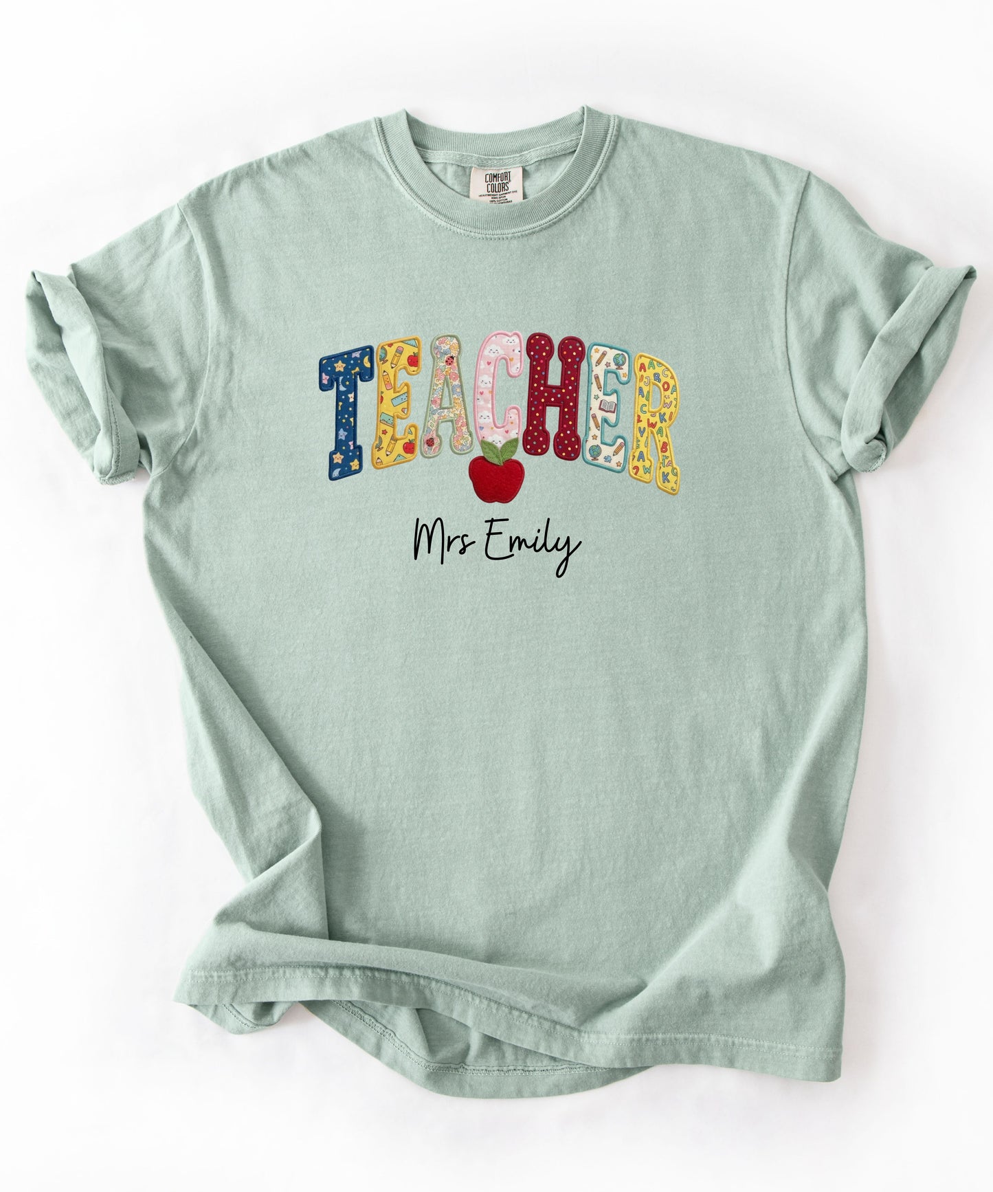 Personalized teacher shirt in Bay with faux patchwork TEACHER lettering, red apple graphic, and custom name — garment-dyed heavyweight tee