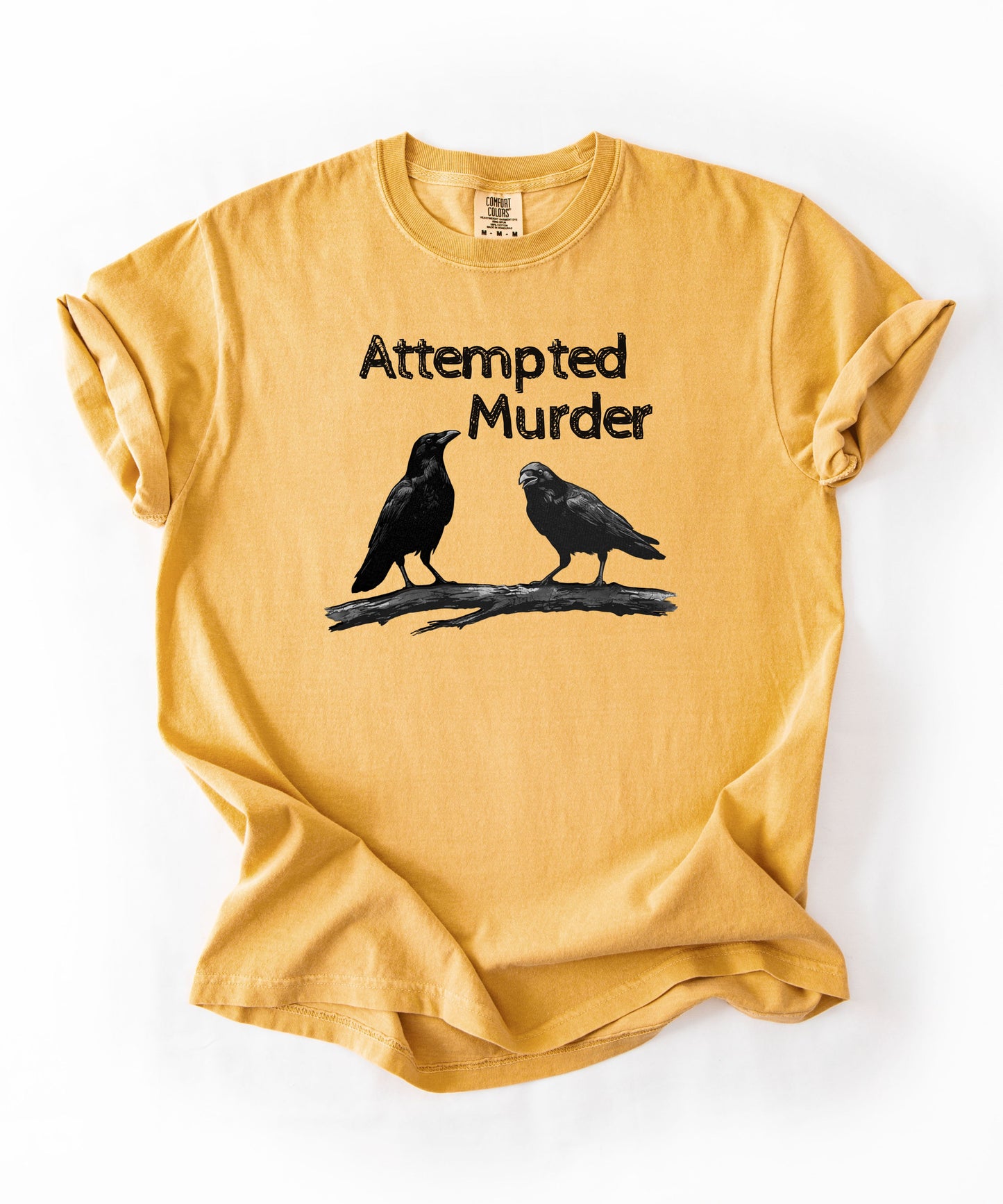 Mustard garment-dyed unisex crow graphic tee — Attempted Murder dark humor bird pun shirt