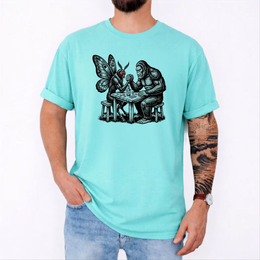 Chalky Mint garment-dyed unisex Bigfoot vs Mothman arm wrestling graphic tee — funny cryptid shirt