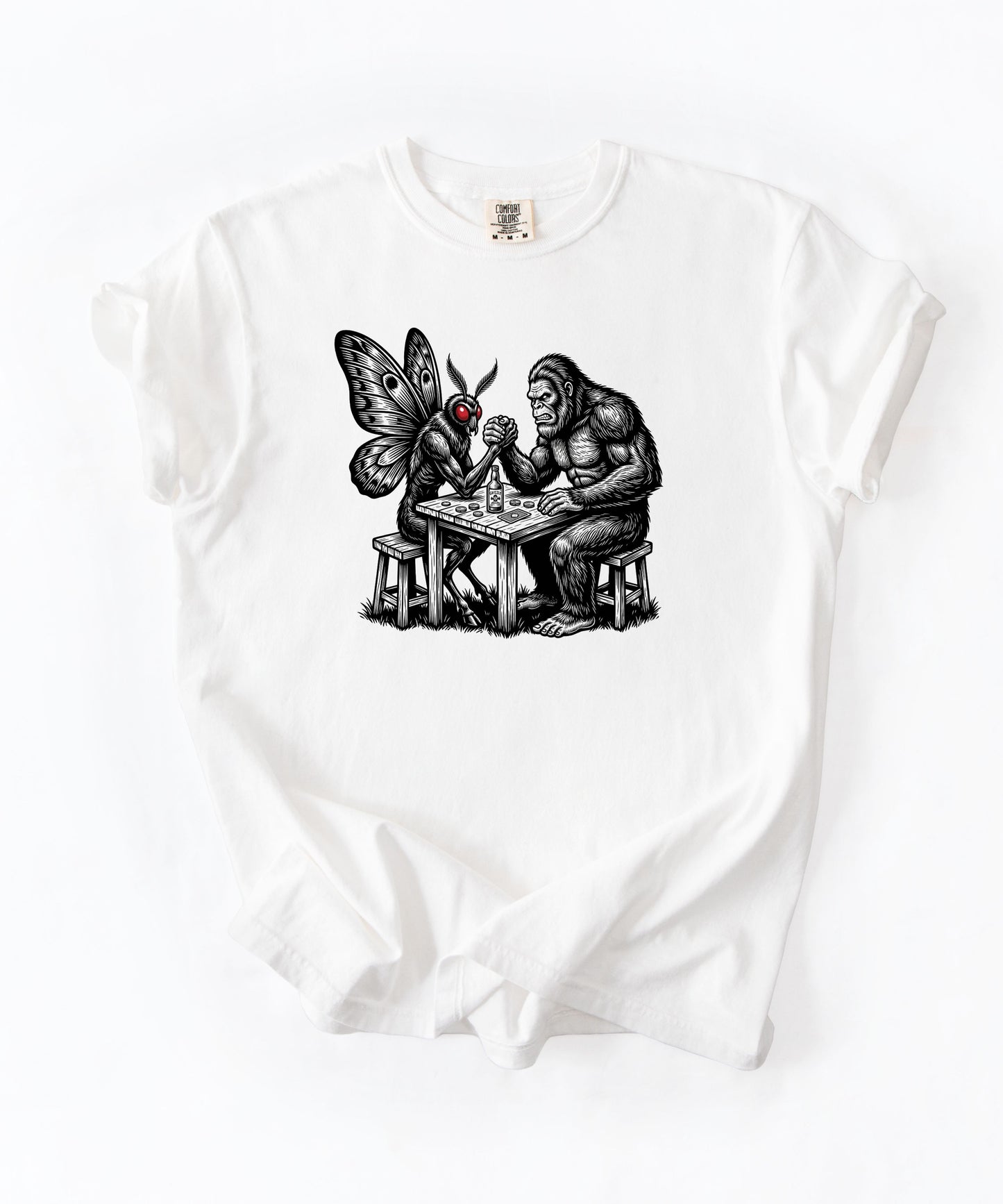 White garment-dyed unisex Bigfoot vs Mothman arm wrestling graphic tee — funny cryptid shirt