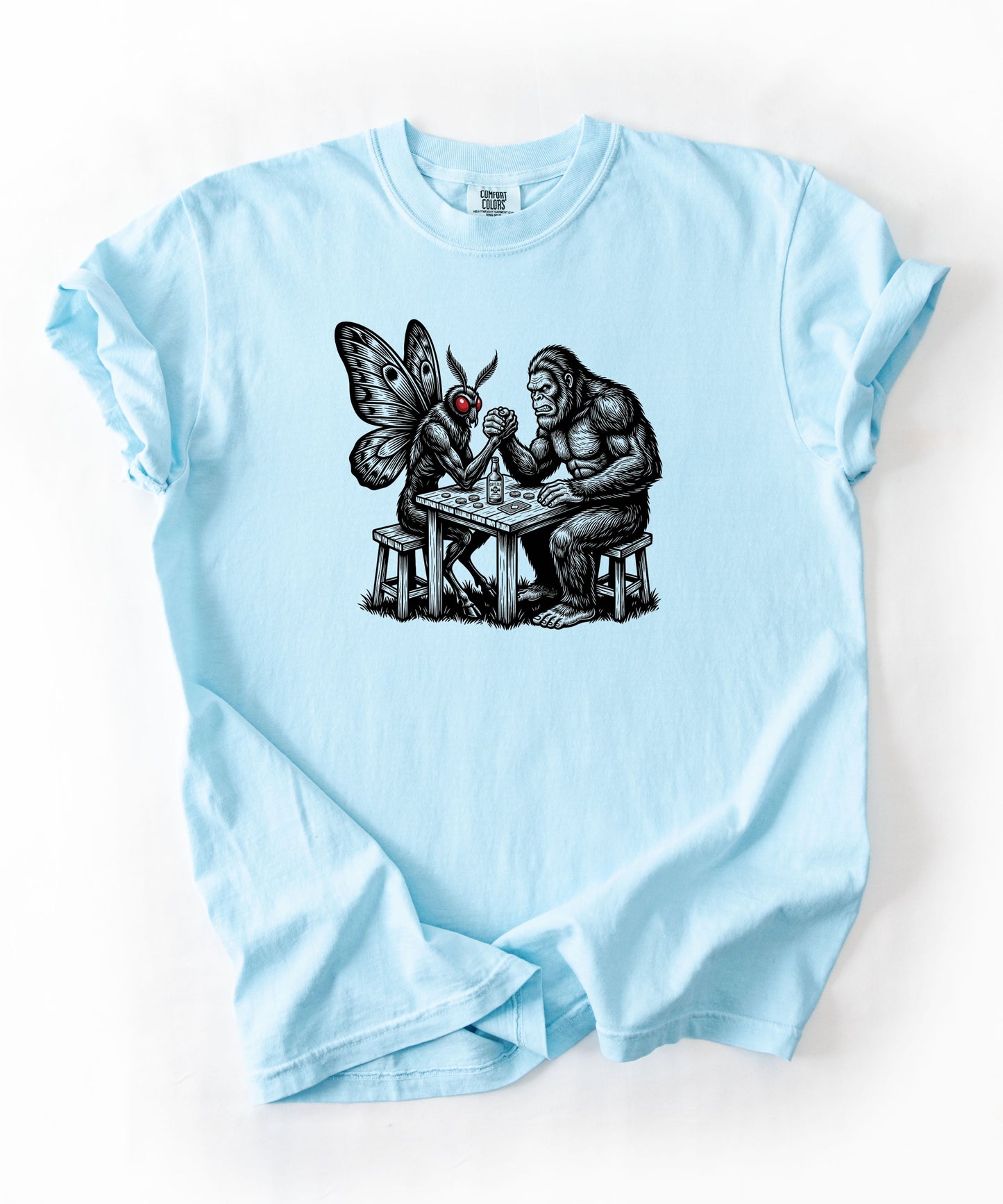 Chambray garment-dyed unisex Bigfoot vs Mothman arm wrestling graphic tee — funny cryptid shirt
