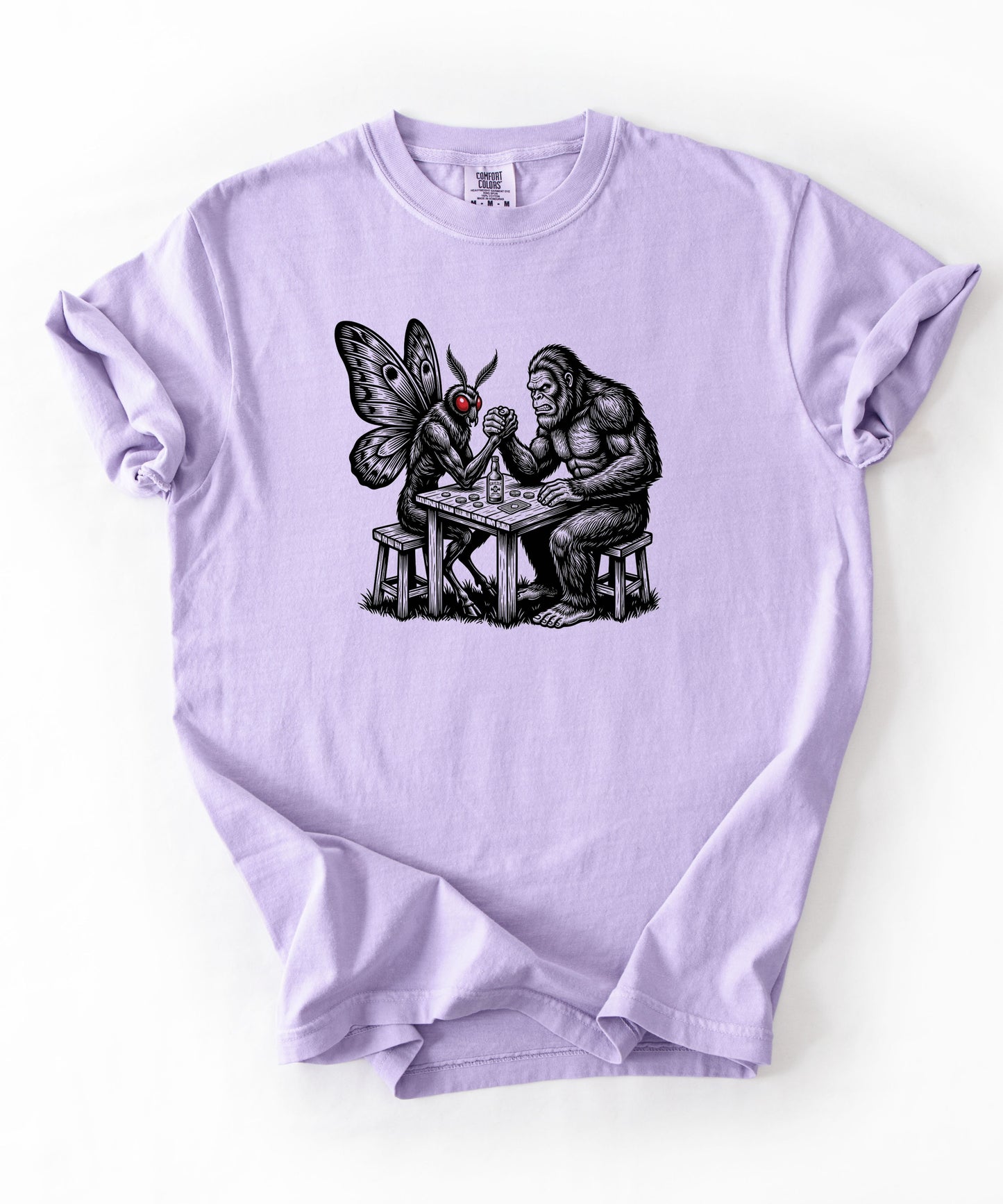 Violet garment-dyed unisex Bigfoot vs Mothman arm wrestling graphic tee — funny cryptid shirt