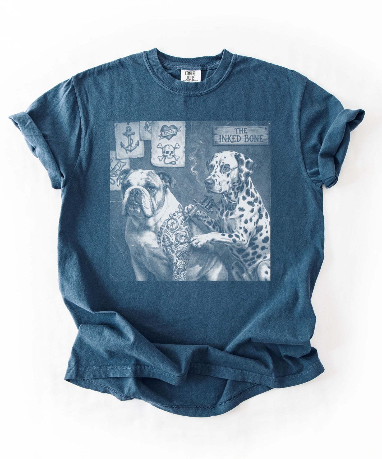 Midnight blue garment-dyed graphic tee laid flat featuring Bulldog and Dalmatian in vintage tattoo shop scene — The Inked Bone design