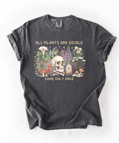 Botanical skull graphic tee featuring herbs, mushrooms, and skull illustration with phrase "All plants are edible, some only once" — front view on garment-dyed cotton Pepper color