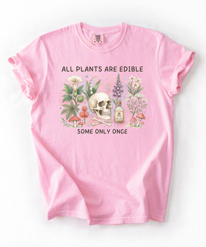 Botanical skull graphic tee featuring herbs, mushrooms, and skull illustration with phrase "All plants are edible, some only once" — front view on garment-dyed cotton Blossom Color