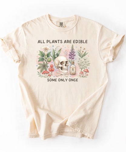 Botanical skull graphic tee featuring herbs, mushrooms, and skull illustration with phrase "All plants are edible, some only once" — front view on garment-dyed cotton Ivory color