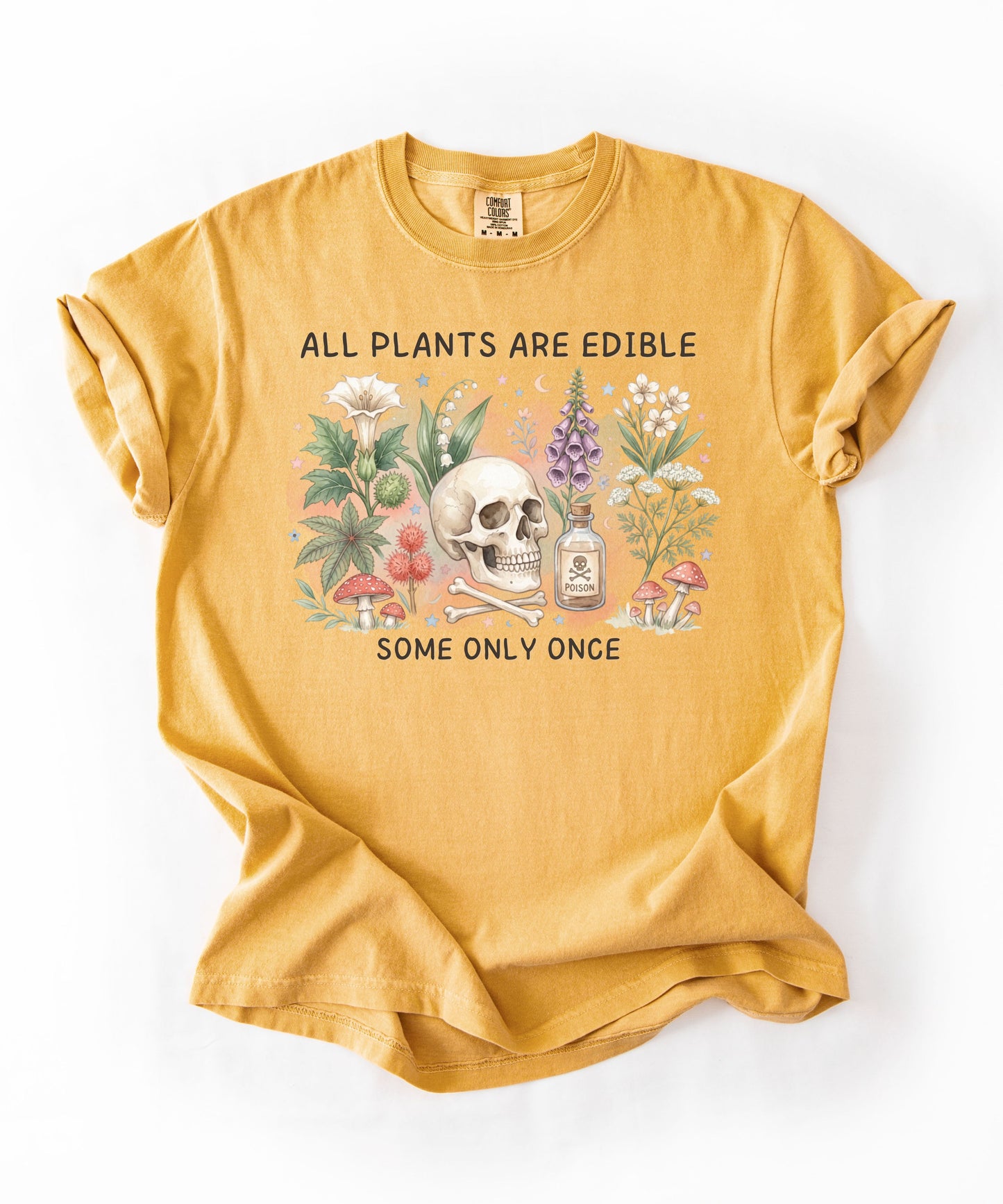 Botanical skull graphic tee featuring herbs, mushrooms, and skull illustration with phrase "All plants are edible, some only once" — front view on garment-dyed cotton Mustard color