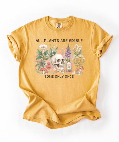 Botanical skull graphic tee featuring herbs, mushrooms, and skull illustration with phrase "All plants are edible, some only once" — front view on garment-dyed cotton Mustard color