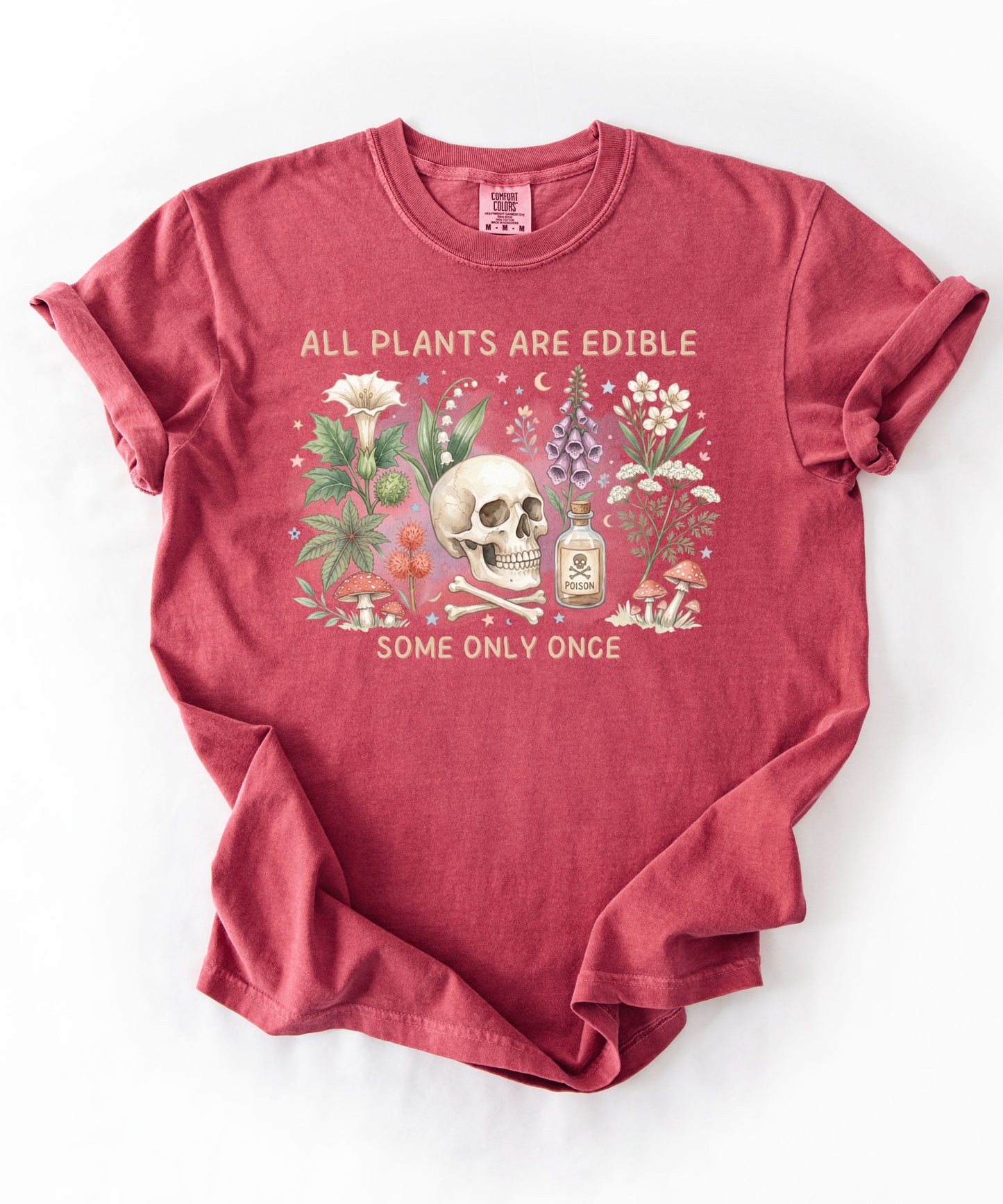 Botanical skull graphic tee featuring herbs, mushrooms, and skull illustration with phrase "All plants are edible, some only once" — front view on garment-dyed cotton Crimson Color