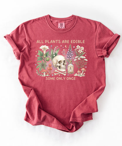 Botanical skull graphic tee featuring herbs, mushrooms, and skull illustration with phrase "All plants are edible, some only once" — front view on garment-dyed cotton Crimson Color