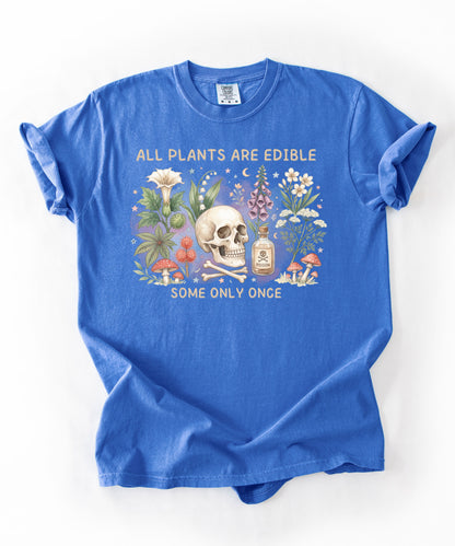 Botanical skull graphic tee featuring herbs, mushrooms, and skull illustration with phrase "All plants are edible, some only once" — front view on garment-dyed cotton Flo blue color