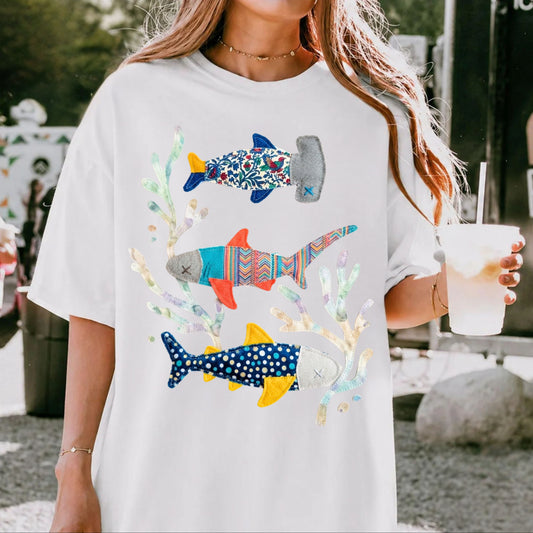 Faux patterned sharks graphic tee in White featuring three hand-painted sharks in muted blues, coral, and botanical swirls — front view on garment-dyed cotton