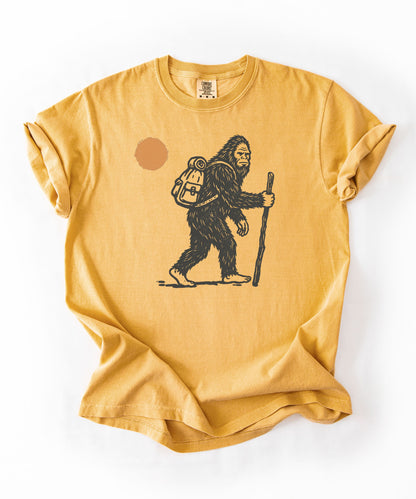 Bigfoot Hiker T-Shirt in Mustard — Sasquatch with backpack sunset graphic tee