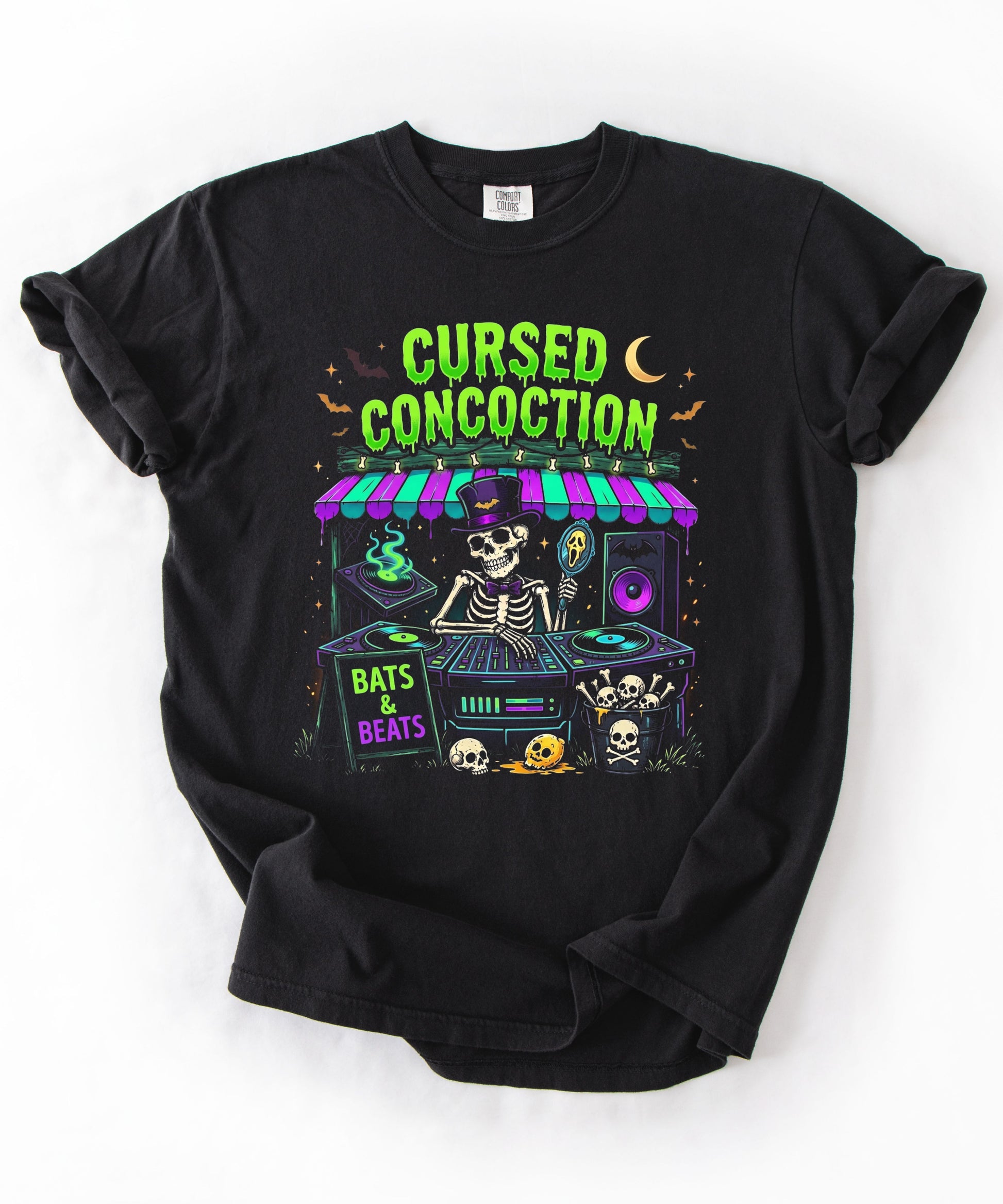 A black short-sleeve t-shirt with a colorful graphic print of a skeleton DJ at a booth under a neon sign that reads 'CURSED CONCOCTION'. The graphic also features 'Bats & Beats' and Halloween-themed illustrations like skulls, bats, and a moon.