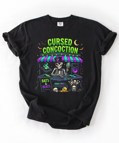 A black short-sleeve t-shirt with a colorful graphic print of a skeleton DJ at a booth under a neon sign that reads 'CURSED CONCOCTION'. The graphic also features 'Bats & Beats' and Halloween-themed illustrations like skulls, bats, and a moon.