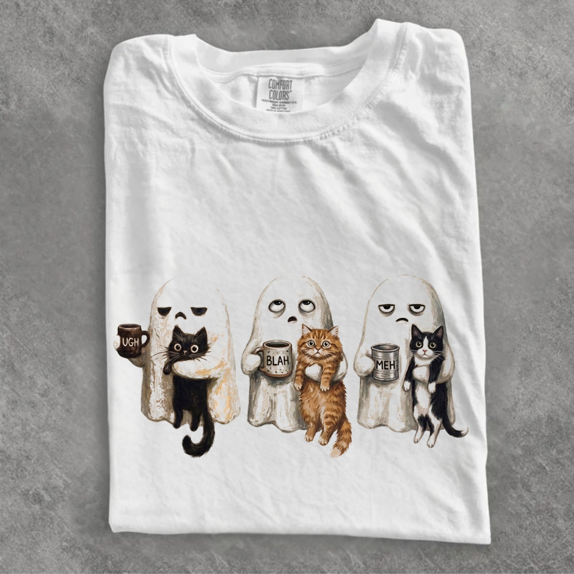 Folded white Ghost Cat graphic tee showing three grumpy ghosts holding cats and UGH BLAH MEH coffee mugs — funny Halloween cat shirt